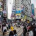 Crowds of people cross street. Tall buildings display election posters.