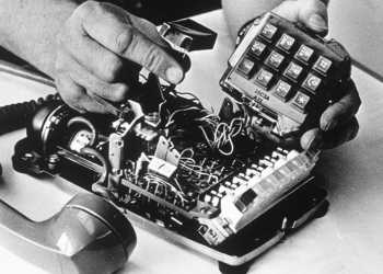 Man's hands placing a wiretap inside an old fashioned telephone