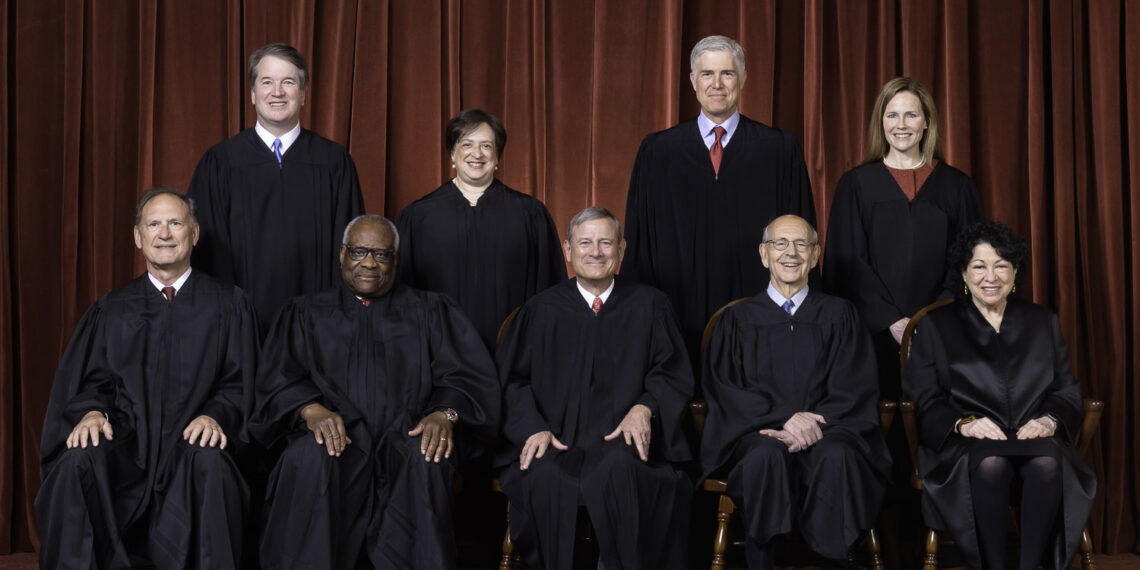 official portrait of nine justices wearing black judicial robes. five justices sit in chairs while four justices stand behind them.