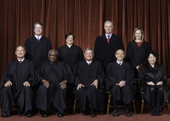 official portrait of nine justices wearing black judicial robes. five justices sit in chairs while four justices stand behind them.