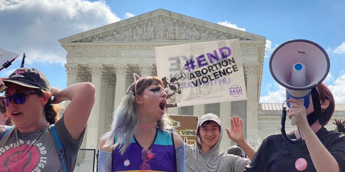 protesters shouting and holding signs in front of supreme court