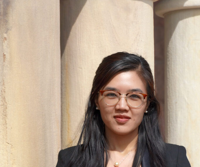 Rosalinn Zahau standing in front of pillars and wearing a black top and black blazer.