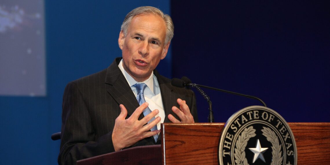 man holds both hands close to chest while speaking behind lectern bearing a texas seal