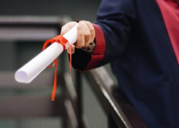 A person dressed in a graduation gown, holding out a diploma.