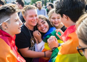 Older children smile and hug while wearing the Pride flag.