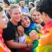 Older children smile and hug while wearing the Pride flag.