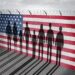 Immigrants behind a wall painted with the American flag and topped with barbed wire