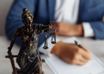 Young man's hands signing a contract with a statue of Lady Justice in the foreground