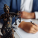 Young man's hands signing a contract with a statue of Lady Justice in the foreground