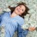 Woman in blue shirt smiling while lying in money