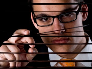 Young man looking through a window blind Spying