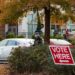 parking lot with "vote here" sign and line of people waiting outside in background