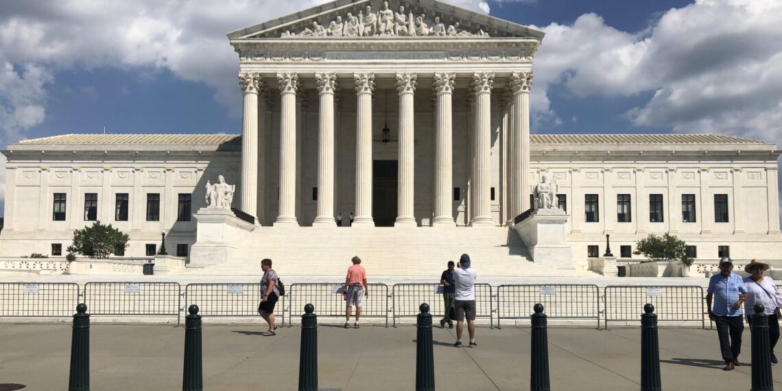 front view of supreme court showing pedestrians occupying sidewalk, with small metal barrier lining steps leading up to the plaza
