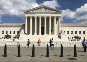 front view of supreme court showing pedestrians occupying sidewalk, with small metal barrier lining steps leading up to the plaza