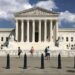 front view of supreme court showing pedestrians occupying sidewalk, with small metal barrier lining steps leading up to the plaza