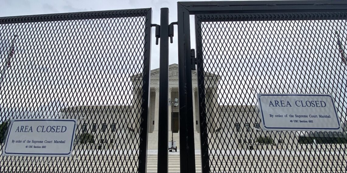 close up photo of chain-link security fence with front of supreme court building visible in background through the fence