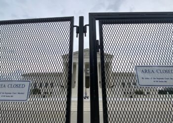 close up photo of chain-link security fence with front of supreme court building visible in background through the fence