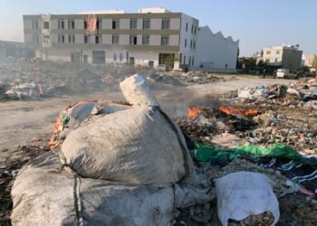 a patch of wasteland with bags of rubbish and fires smouldering