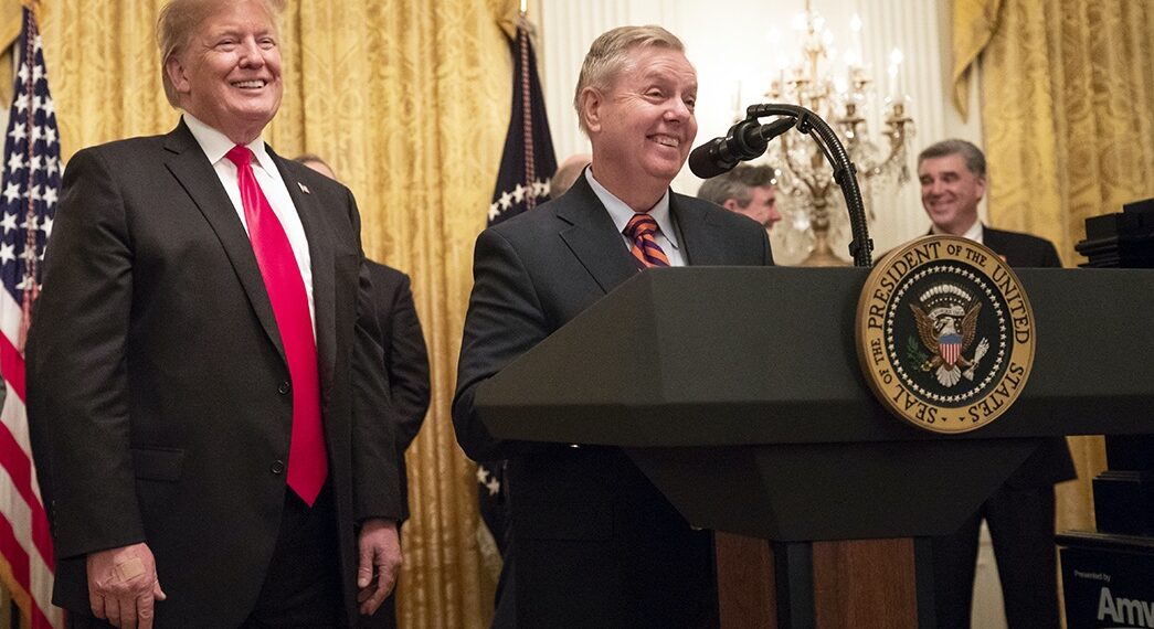 lindsey graham smiles while standing at lectern bearing presidential seal. donald trump stands alongside.