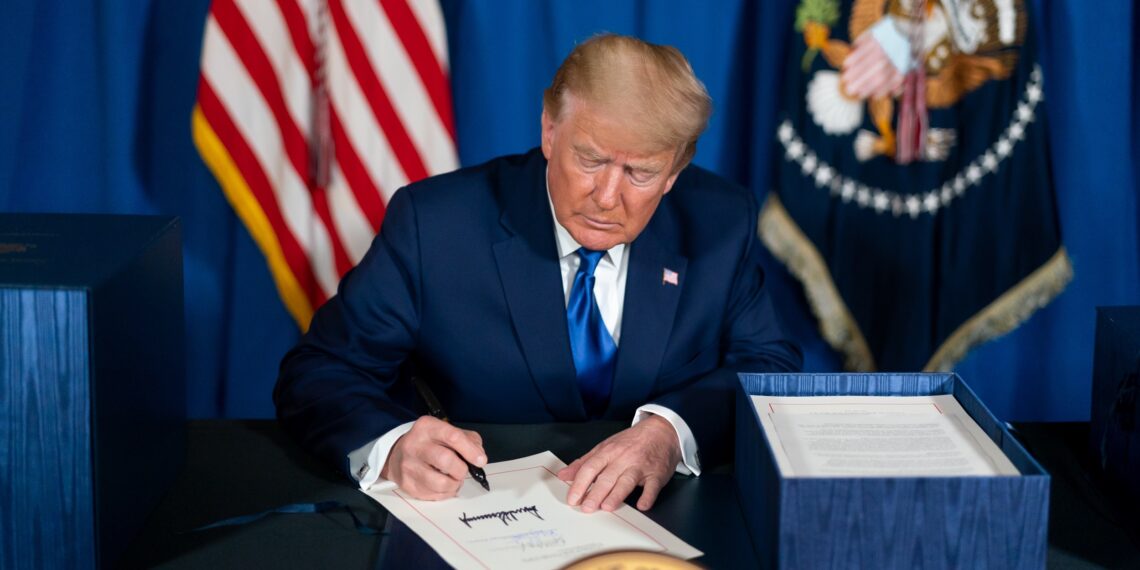 president trump sitting at desk and signing a document