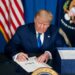 president trump sitting at desk and signing a document