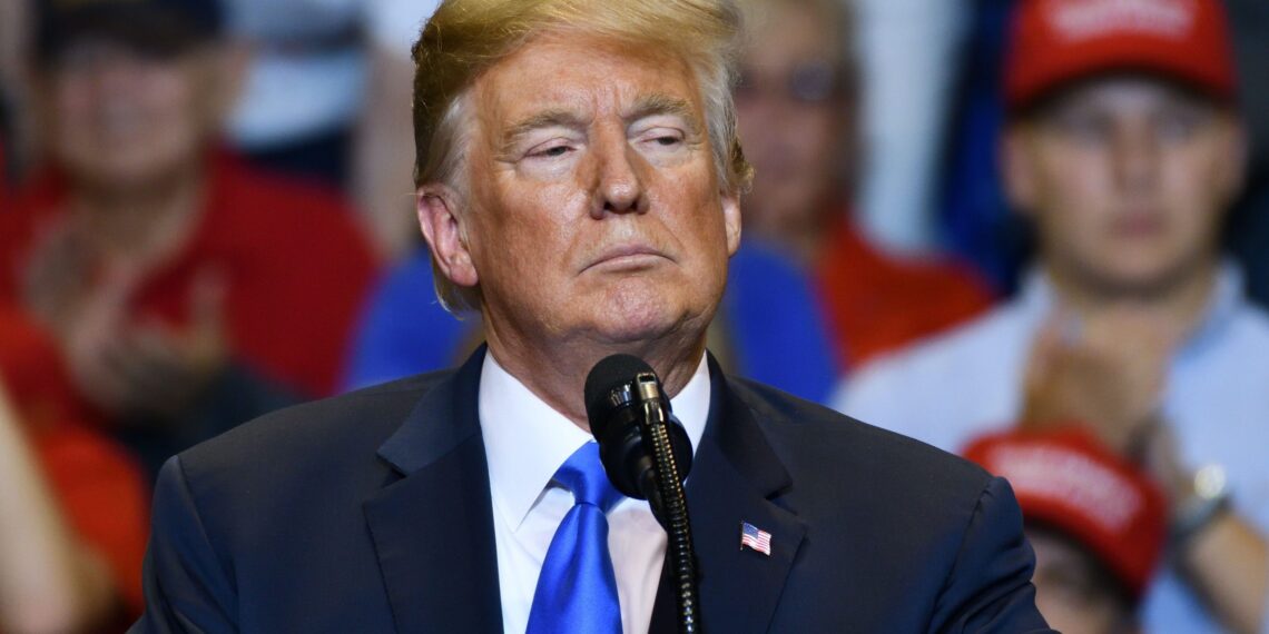 donald trump standing in front of microphone with serious look and crowd of people in background