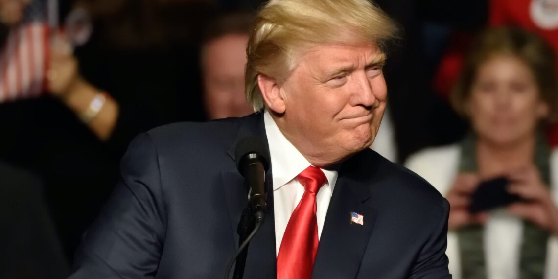 donald trump stands before microphone and looks to the right while grimacing