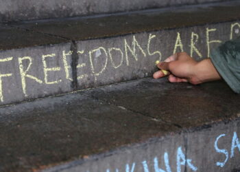 Image shows a person writing the word freedoms using chalk on a concrete staircase.