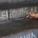 Image shows a person writing the word freedoms using chalk on a concrete staircase.