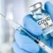 Hand in blue medical gloves holding a syringe and vaccine vial with Covid 19 Vaccine Booster text, for Coronavirus booster shot.