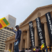 Protestor waving Sri Lankan flag in front of imposing government building.