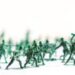 Many green army plastic toy soldiers organized on top of a white surface and background, isolated, with out of focus plastic soldiers in the background