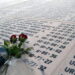 Flowers resting atop white marble covered with names and dates.