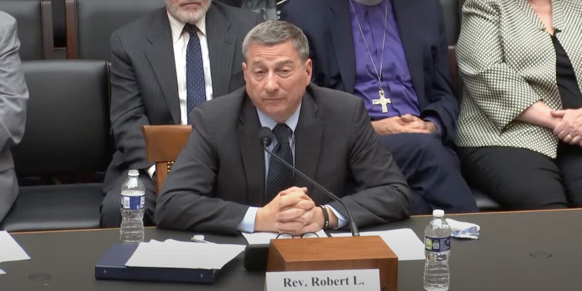 Man speaking into microphone at desk.