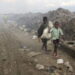Two children in tattered clothes walk through a trash dump