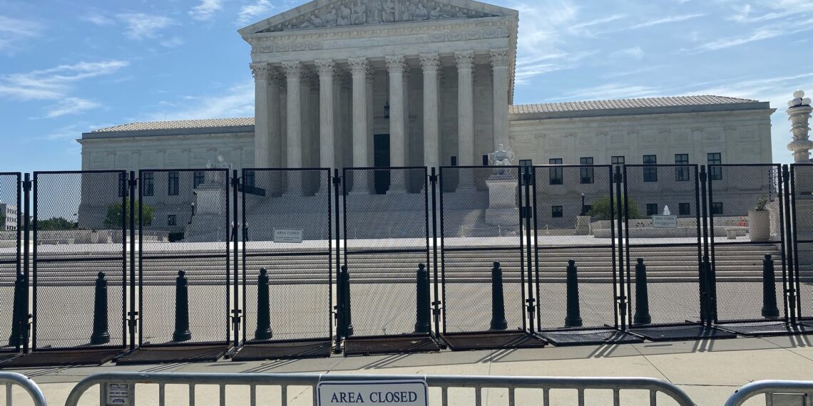 tall black fence and a gate bearing an "area closed" sign stand in front of the supreme court building