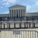 tall black fence and a gate bearing an "area closed" sign stand in front of the supreme court building