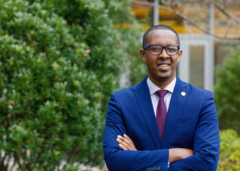 Benyam Dawit Mezmur wearing a blue suit and standing in front of trees with his arms crossed.