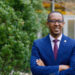 Benyam Dawit Mezmur wearing a blue suit and standing in front of trees with his arms crossed.