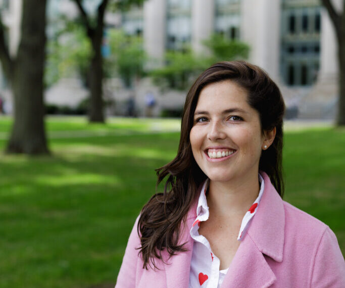 Maria Cecilia Ercole wearing a pink coat and smiling into the camera while standing in front of Harvard Law Langdell Library.