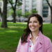 Maria Cecilia Ercole wearing a pink coat and smiling into the camera while standing in front of Harvard Law Langdell Library.