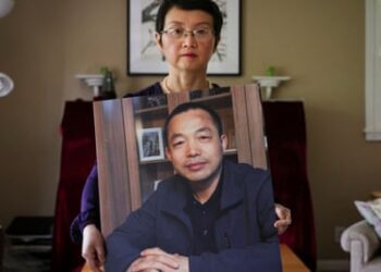 Luo Shengchun, the wife of Ding Jiaxi, poses with a photo of her husband at her home in Alfred, New York, last year
