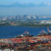 aerial view of busy seaport crowded with containers. a body of water separates the port in the foreground from the manhattan skyline in the background.