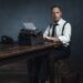 Retro 1940 office worker behind desk with typewriter and telephone.