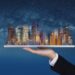 Real estate business, smart city, and building technology. Businessman hand holding digital tablet with buildings hologram and stars background