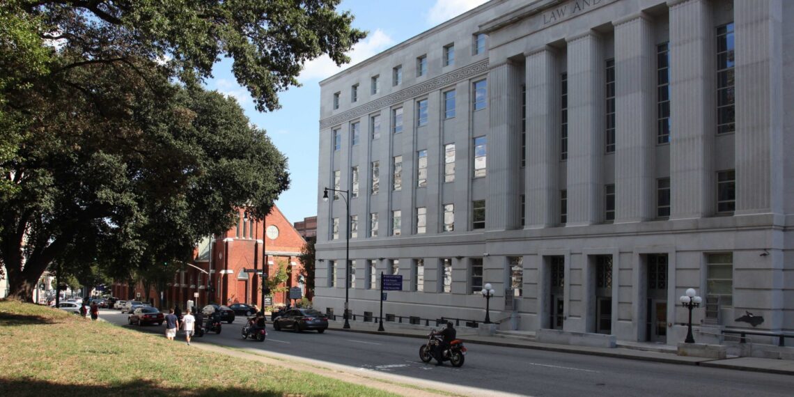 A large grey building with "Law and Justice" carved into the stone at the top, across the street is a grassy park.