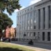 A large grey building with "Law and Justice" carved into the stone at the top, across the street is a grassy park.