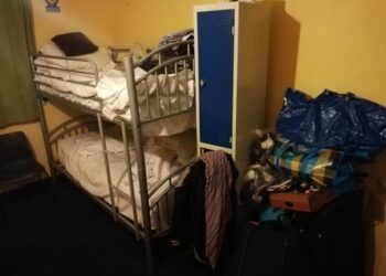 Two bunk beds in a room next to a small cupboard with personal belongings piled up all around it