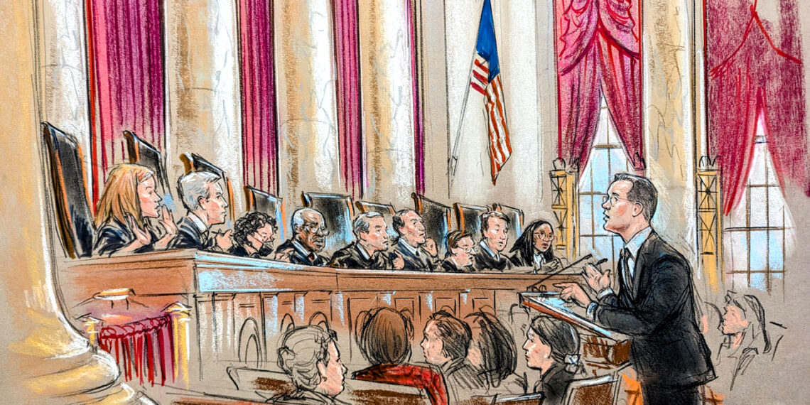 A man speaks to the full bench of justices from the lectern. A seated crowd listens.