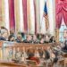 A man speaks to the full bench of justices from the lectern. A seated crowd listens.